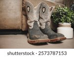 Weathered, muddy boots by a timeworn couch evoke rustic warmth and nostalgia. Perfect for storytelling, lifestyle, or creative campaigns, this high-quality photo captures timeless journeys.