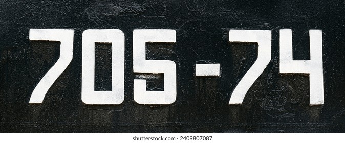 Weathered numbers 7, 0; 5, 4, seven, zerro, five, four, or 70574 painted white on a piece of black metal. Abstarct numeral background for design.
