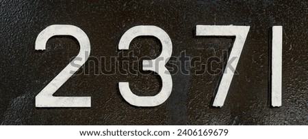 Weathered numbers two, three, seven; one; 2371 or 2, 3, 7, 1 painted white on a piece of black metal. Abstarct numeral background for design.