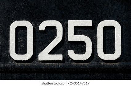 Weathered numbers zero, two, five, 0250, or 0, 2, 5 painted white on a piece of black metal. Abstarct numeral background for design.