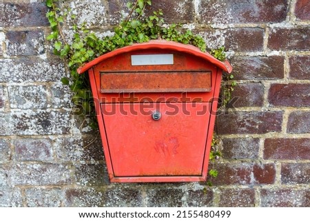 Weathered orange post box with silver lock surround by ivy on a red brick wall
