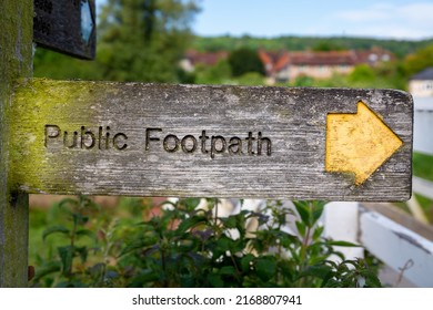 Weathered public footpath sign featuring a yellow arrow indicating a public right of way in a rural location