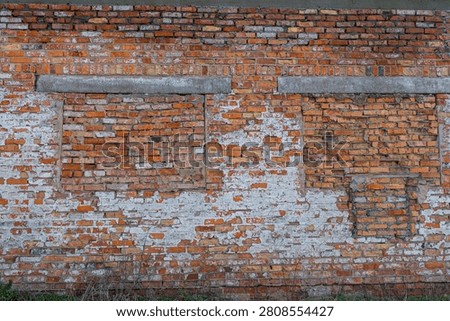 Weathered red brick wall with bricked-up windows and remnants of peeling white plaster.