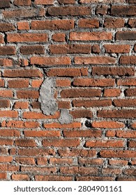 Weathered red brick wall featuring rough textures, aged mortar, and subtle patches of cement repair. The warm earthy tones of the bricks, combined with the strong natural sunlight, emphasize the wall’s rustic character and architectural detail. This full-frame image is ideal as a background texture for construction, renovation, industrial, or vintage design projects.