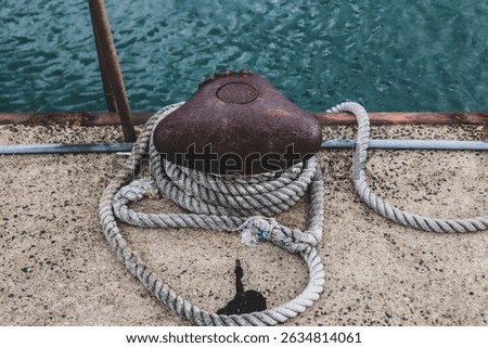Weathered rope coiled around a rusty bollard on a seaside pier — a quiet moment by the harbor, where time and tide leave their mark.
