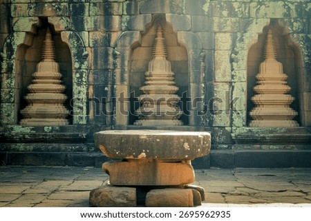 A weathered stone altar stands before intricately carved temple walls featuring three arched niches, each housing a tiered stupa.