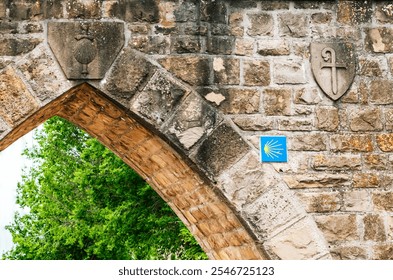 A weathered stone arch displays historical emblems and a Camino marker. - Powered by Shutterstock