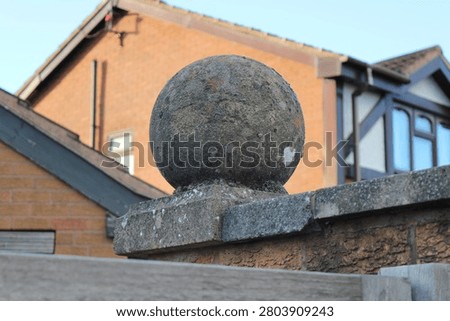 Weathered Stone Ball On Gatepost With Residential Brick House In Suburban Garden Setting