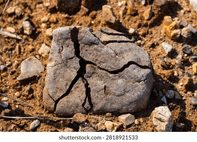 Weathered stone boulder with deep cracks lying on dry parched ground, close-up of geological erosion and natural rock fracturing in a harsh arid desert environment