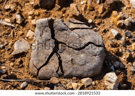 Weathered stone boulder with deep cracks lying on dry parched ground, close-up of geological erosion and natural rock fracturing in a harsh arid desert environment