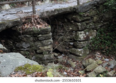 A weathered stone bridge spans a tranquil stream, embraced by lush greenery and autumn leaves. This peaceful spot invites exploration and reflection. - Powered by Shutterstock