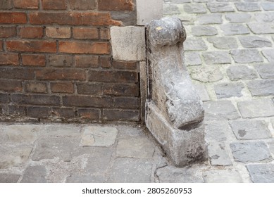 Weathered stone corner support structure is affixed to a brick wall on a cobblestone street, highlighting architectural features and historical context