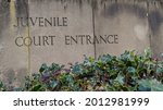 Weathered stone slab sign with the words juvenile Court Entrance engraved into it with foliage at the bottom Outside the Department Of Justice courthouse where juveniles are tried. 
