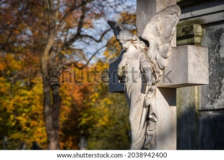 A weathered stone statue of praying angel on grave in Brompton Cemetery during autumn 