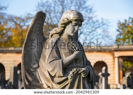 A weathered stone statue of praying angel on grave in Brompton Cemetery in London