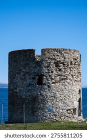 a weathered stone windmill base or round tower ruin on the coast of Nessebar, set against the deep blue water of the Black Sea and a clear sky.