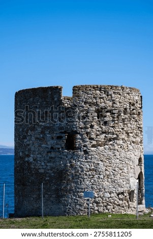 a weathered stone windmill base or round tower ruin on the coast of Nessebar, set against the deep blue water of the Black Sea and a clear sky.
