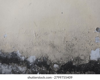 A weathered wall with a beige surface, displaying significant dirt and grime accumulation towards the lower section. The wall shows signs of wear, with peeling paint and blackened patches indicative of moisture damage or mold growth. The texture varies from smooth at the top to rough and uneven at the bottom, creating an aged and distressed appearance. The overall condition of the wall suggests longstanding exposure to environmental elements.