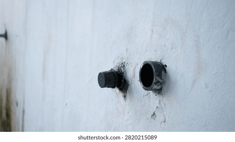 Weathered wall shows two pipe openings. One cap sits loose, the other is missing. Mildew and cracks hint at neglect. Industrial decay and time wear are evident. Ideal for construction, urban decay