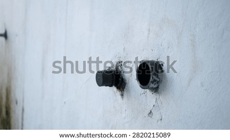 Weathered wall shows two pipe openings. One cap sits loose, the other is missing. Mildew and cracks hint at neglect. Industrial decay and time wear are evident. Ideal for construction, urban decay