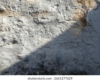Weathered wall surface with sunlight and shadow cracked old plaster texture with natural earthy tones and rough details, suitable for grunge backgrounds or abstract design elements

