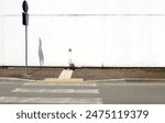 Weathered white concrete wall with air intake. Sidewalk, pedestrian crossing sign, crosswalk and urban street in front. Background for copy space.