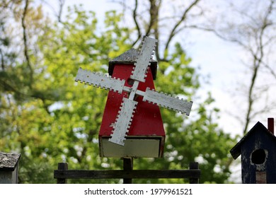 A Weathered, Windmill Shaped Bird House. The Painted Bird House Is Made Of Wood And Covered In Red, White, And Blue Paint Making The Nesting Area Look Patriotic.