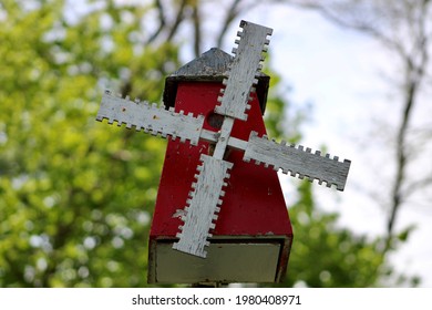 A Weathered, Windmill Shaped Bird House. The Painted Bird House Is Made Of Wood And Covered In Red, White, And Blue Paint Making The Nesting Area Look Patriotic.