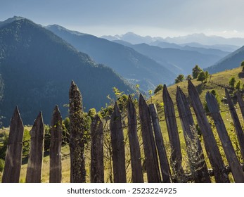 A weathered wooden fence in the foreground, framing a stunning view of lush green hills and layered mountain ranges in the distance under a clear sky. - Powered by Shutterstock