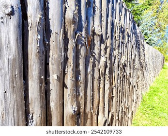 A weathered wooden fence stretches along a vibrant green field, highlighting the natural textures of the aged wood under bright sunlight. - Powered by Shutterstock