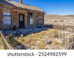 A weathered wooden house with porch in Bodie ghost town, California. The abandoned frontier homestead showcases preserved Wild West architecture against a barren desert landscape.