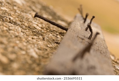 A weathered wooden plank with  rusty nails sticking out, lying on a concrete surface with some rocks and debris. - Powered by Shutterstock