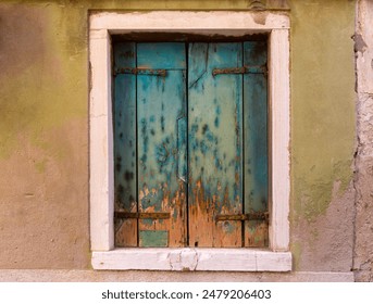 A weathered wooden shuttered window with peeling paint on an old building facade in Venice, Italy - Powered by Shutterstock