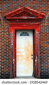 Weathered, Worn And Dilapidated Doorway Has Broken Door Frame And Peeling Red Paint.  Building Is Black And Red Brick.