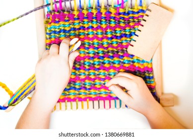 Weaving. Hands of little caucasian girl holdig a shuttle. Working on small loom weaving. Close-up photo isolated on white background.