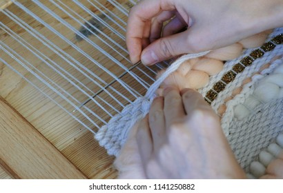 Weaving on a loom. Weaving on a loom. Closeup woman's hands running on a loom. Threading the needle through the strands of frame.