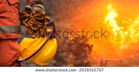 Web banner concept firefighter team, Safety helmet and heat resistant gloves on hand holding after duty on background with professional team firefighter working spraying high pressure water to fire.