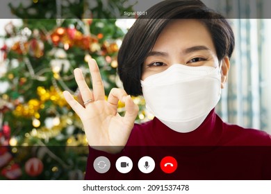 Web Cam Video Call Shot Mock Up. A Beautiful Asian Woman In Red With Medical Face Mask Happy Smiling And Do Okay Hand Sign To Her Friends And Family Through Online Chat Application On Christmas Eve.