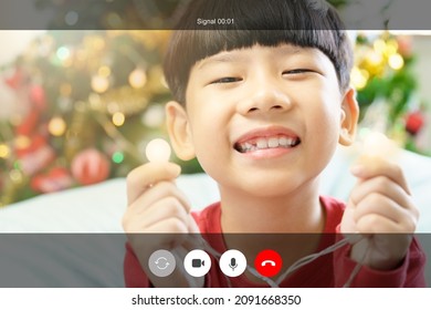 Web Cam Video Call Shot Mock Up. An Adorable Asian Little Boy In Red Sit In Front Of A Bright And Full Decoration Christmas Tree Cheerful Smiling To Family Through Online Chat Application On Christmas