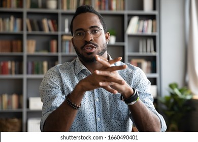 Web cam view serious concentrated young african ethnic businessman in eyeglasses holding video call negotiations with partners. Focused multiracial male job seeker talking to hr manager online.
