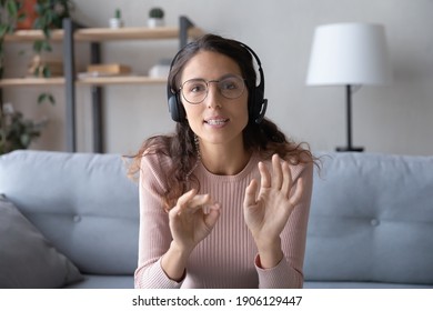 Web camera view smart young caucasian woman in eyeglasses wearing headset with microphone, holding distant negotiations meeting with colleagues from home or giving educational online lecture.