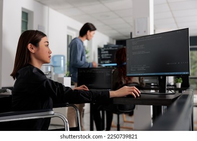 Web developer in wheelchair working on server coding in big data office, analyzing programming language and script on terminal window. Disabled woman programmer with impairment working on it system.