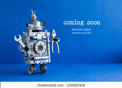 Web site under construction Coming Soon page. Toy robot with hand wrench and pliers. Blue background