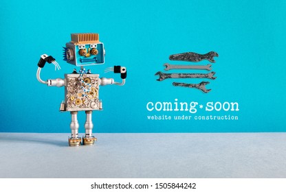 Web site under construction Coming Soon template page. Toy robot looks at a set of hand wrenches for maintenance repairs and service works. Blue wall and copy space on gray background
