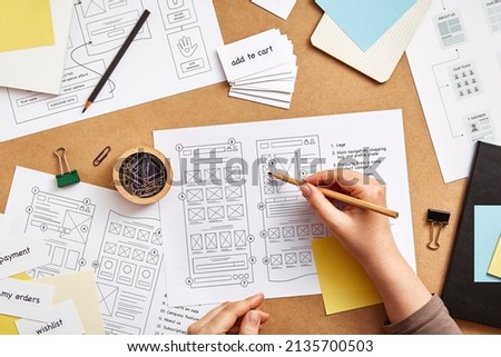Web UX designer working at desk with several website wireframe sketches and sitemap. Website project concept. Flat lay