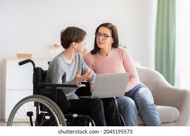 Web-based Education Concept. Cheerful Disabled Teen Boy In Wheelchair, Making Home Assignment With His Mom, Using Laptop Indoors. Smart Youth Studying With Private Tutor