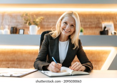Webcam headshot of sociable positive beautiful caucasian mature business woman, business owner, sit at table, video calling with colleagues, partners, looking at camera, taking notes, smiles friendly - Shutterstock ID 2095030063