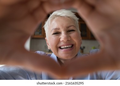 Webcam portrait happy smiling old age lady kind loving granny look at camera in finger heart express love to grandchild. Grateful older woman shoot selfie to thank children or doctor at virtual space