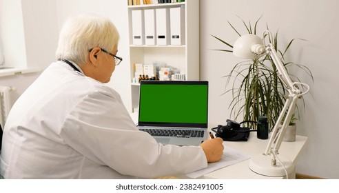 Webinar watched by woman doctor on green screen laptop. Female in medicare talking to patients online taking notes of symptoms. - Powered by Shutterstock