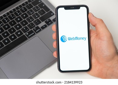 WebMoney financial platform for money transfer using smartphone. Man hand holding a mobile phone with application on the screen and notebook on the background. November 2021, San Francisco, USA
